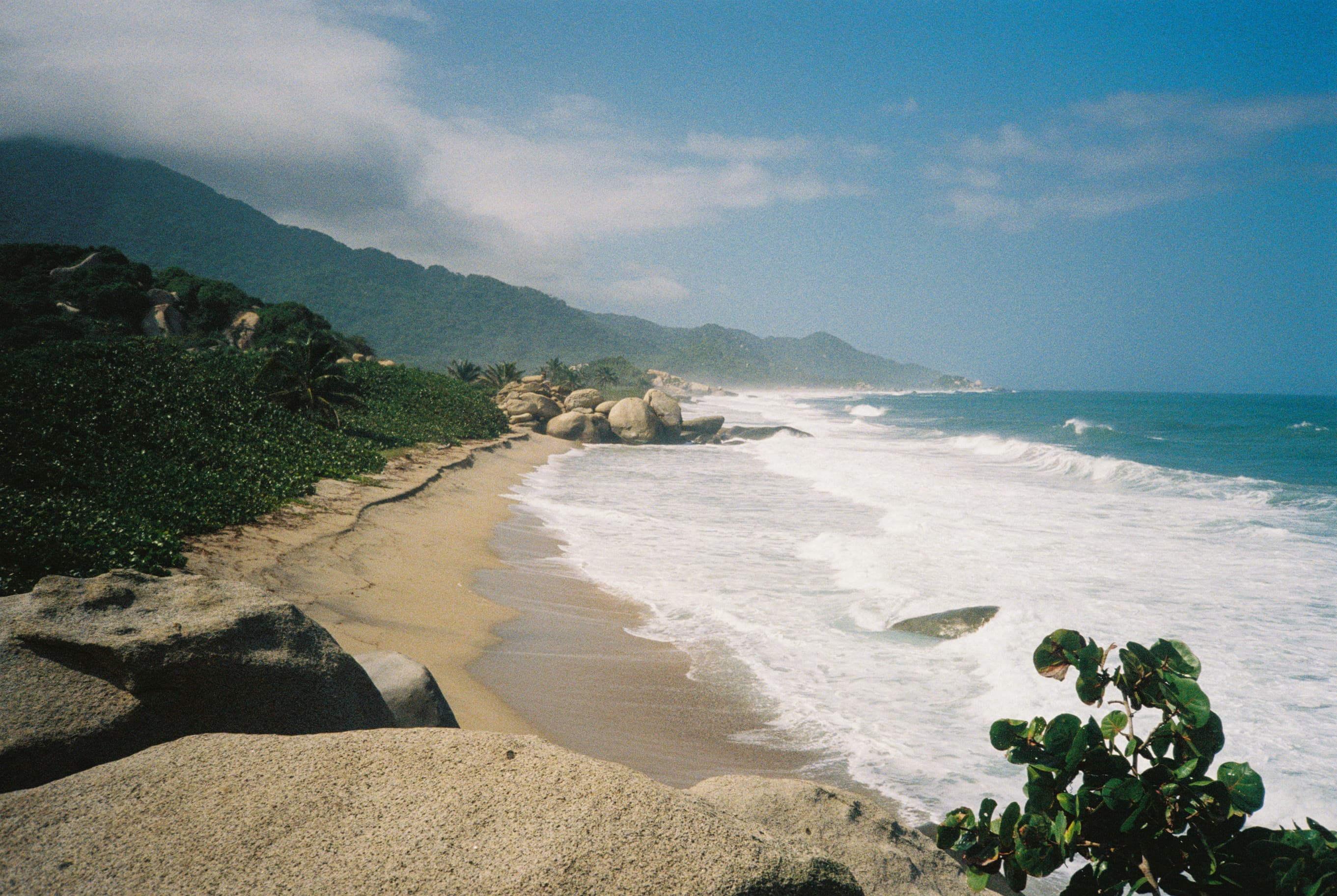 Photo of the beach in tayrona. In the background big egg shaped rocks can be seen. The sea has strong waves.